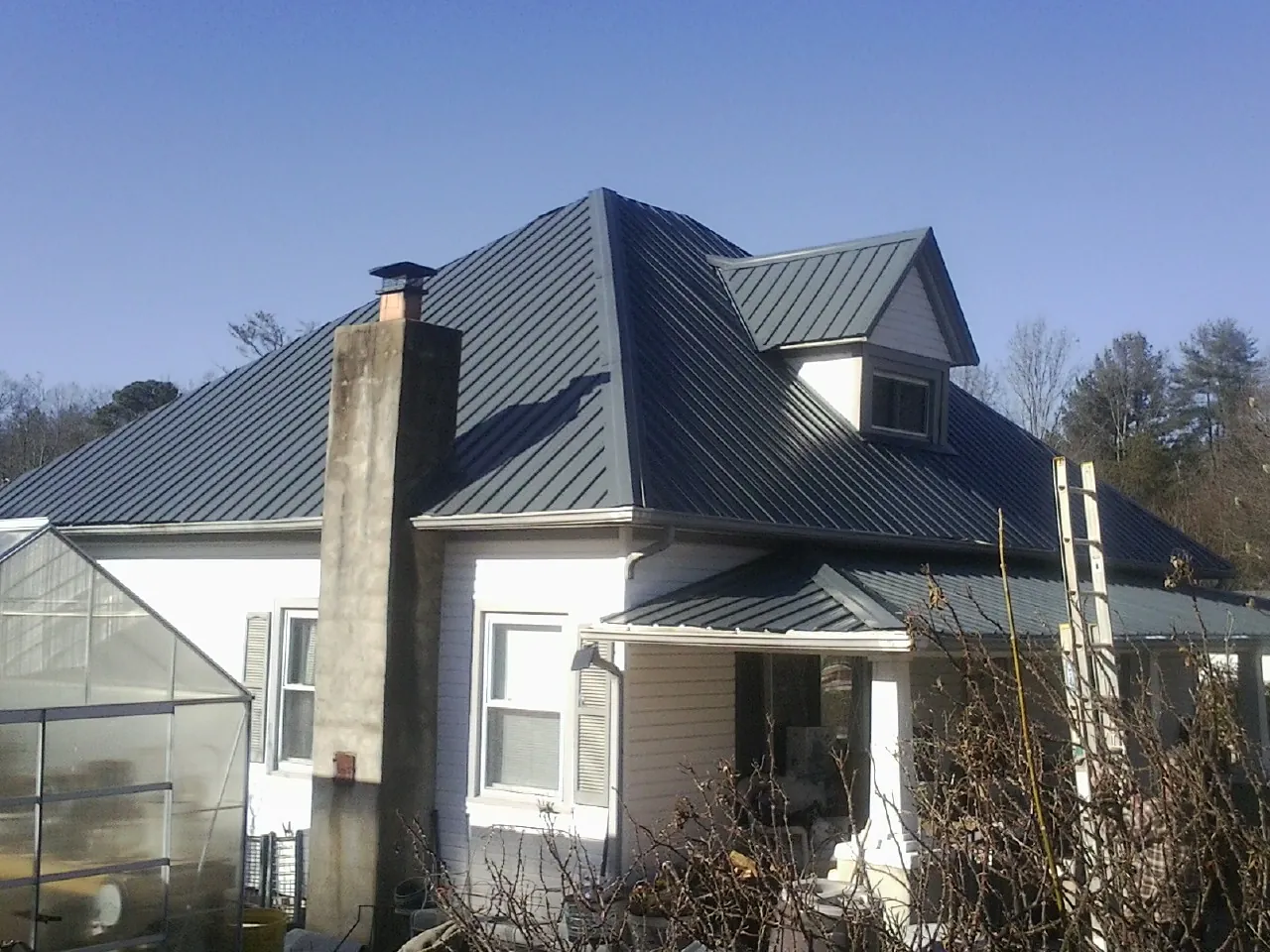 Dark blue standing seam metal roof on a white farmhouse with dormer — Slate & Tile Roof Repair by Roofing Brothers in Teeds Grove