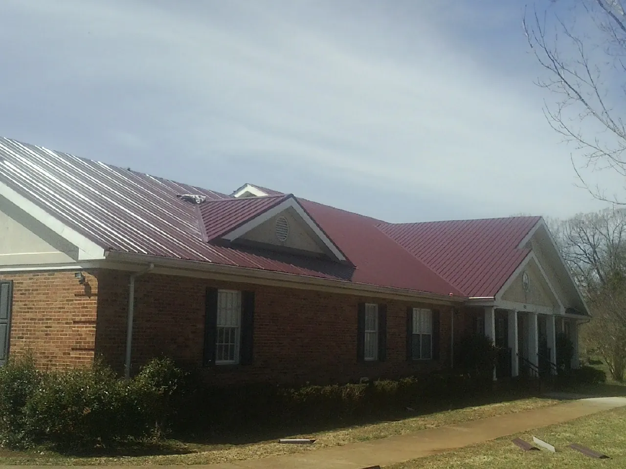 Red metal roof with gabled entries on a long brick building, from a Hail Damage Roof Repair job in Teeds Grove