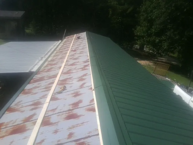 Old rusted panels beside newly installed green metal roofing — Wind Damage Roof Repair by Roofing Brothers in Teeds Grove