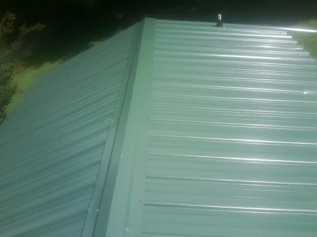 New green metal panels meeting at the ridge of a roof — Flat Roof Repair work by our crew in Teeds Grove