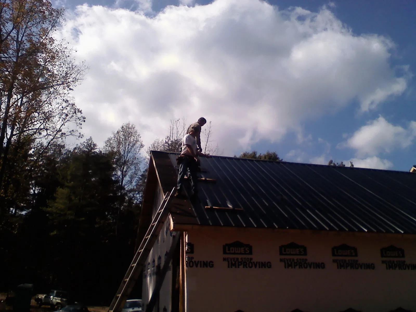 Roofer fastening dark metal panels high against a cloudy sky, from a Roof Inspection job in Teeds Grove