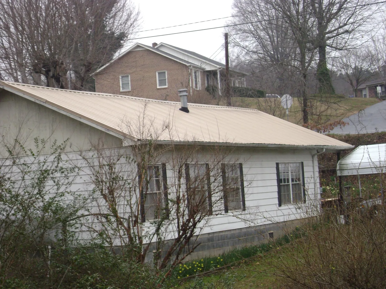 Tan metal roof on a white sided house set into a hillside — Commercial Roofing by Roofing Brothers in Teeds Grove