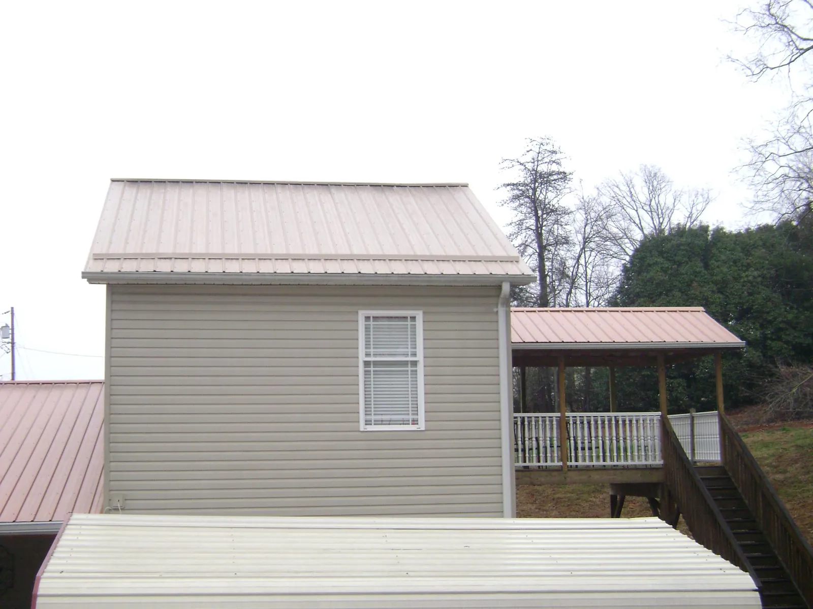 Tan metal roofs on a two story addition and attached porch, from a Roof Replacement job in Teeds Grove