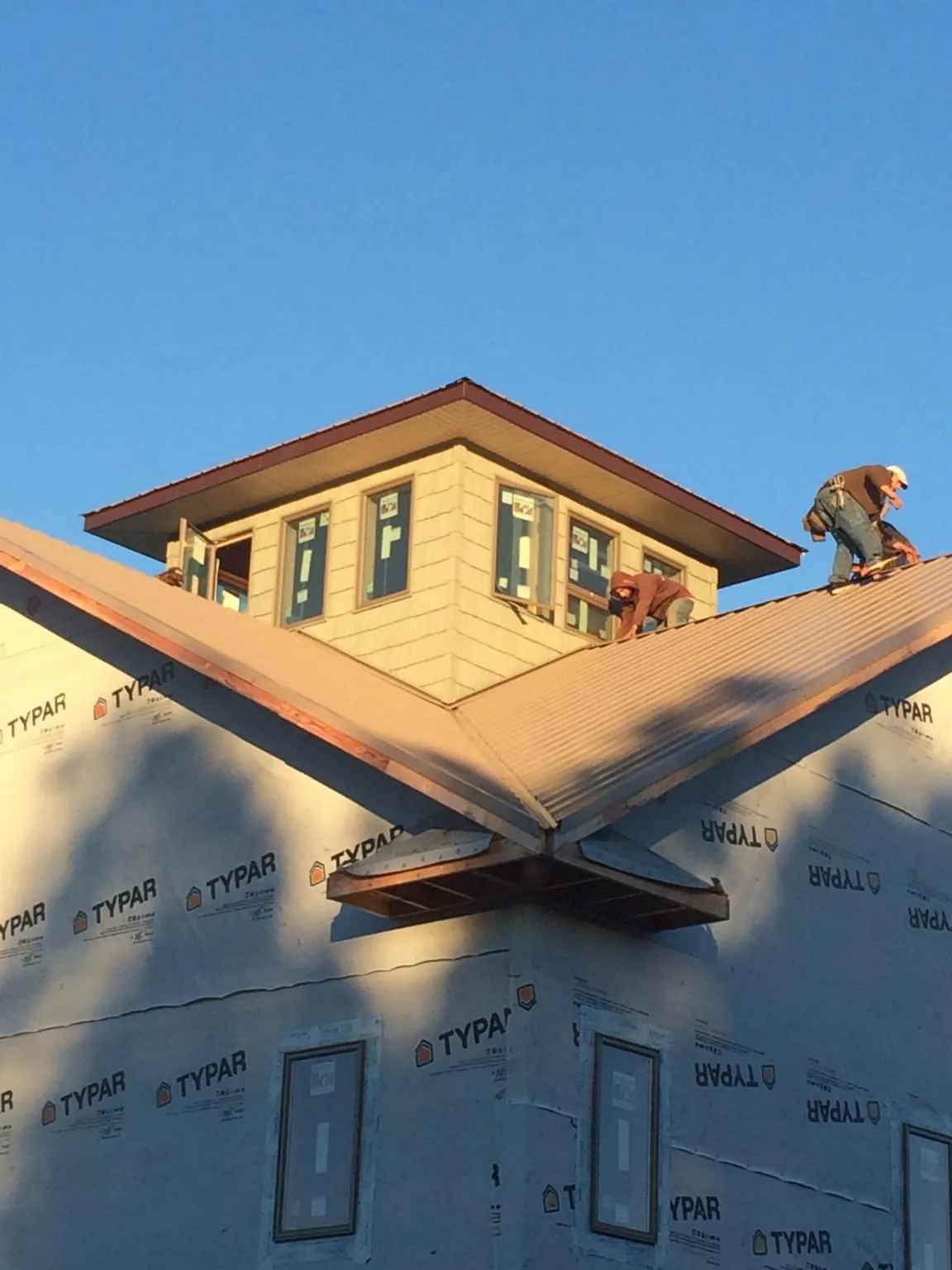 Roofers working around a rooftop cupola on a new metal roof at sunset — Roof Waterproofing in Teeds Grove by Roofing Brothers